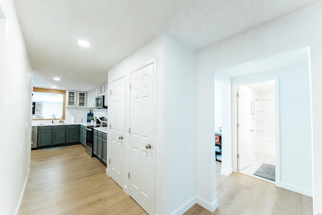 kitchen with light wood-style flooring, range with electric cooktop, light countertops, stainless steel microwave, and glass insert cabinets