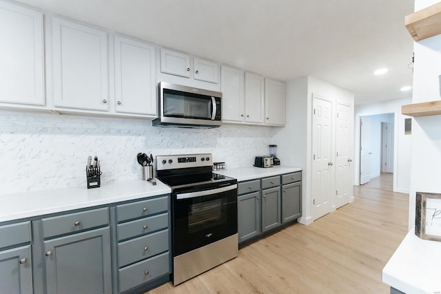 kitchen with light countertops, appliances with stainless steel finishes, light wood-type flooring, gray cabinets, and decorative backsplash