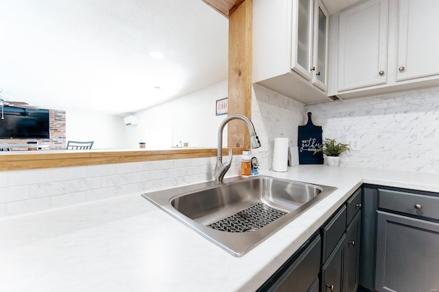 kitchen with tasteful backsplash, glass insert cabinets, light countertops, and a sink