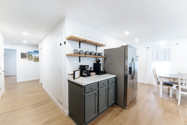 kitchen featuring gray cabinetry, light wood-style floors, light countertops, stainless steel refrigerator with ice dispenser, and open shelves