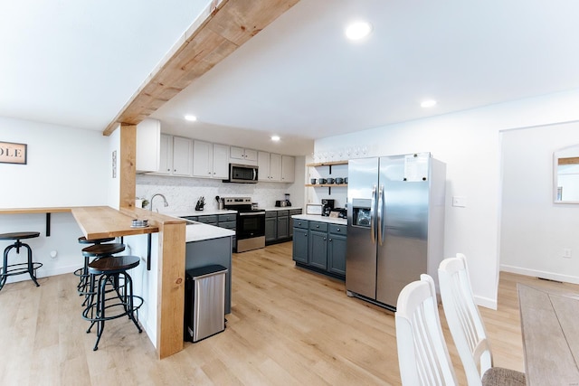 kitchen with light countertops, light wood-style flooring, decorative backsplash, appliances with stainless steel finishes, and a kitchen breakfast bar