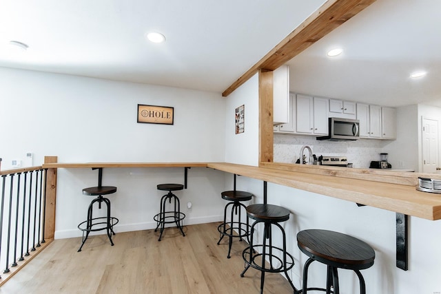 kitchen with stainless steel microwave, backsplash, white cabinetry, light wood-type flooring, and a peninsula