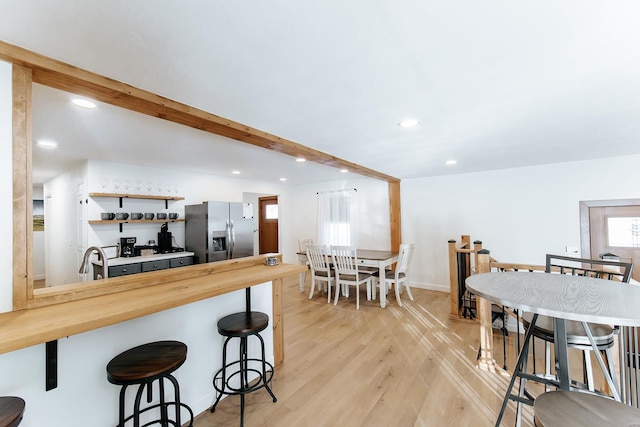 kitchen with wood counters, a breakfast bar area, stainless steel refrigerator with ice dispenser, and beamed ceiling