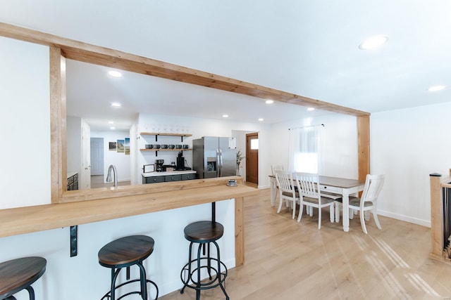 kitchen with beamed ceiling, a kitchen bar, wood counters, and stainless steel fridge with ice dispenser