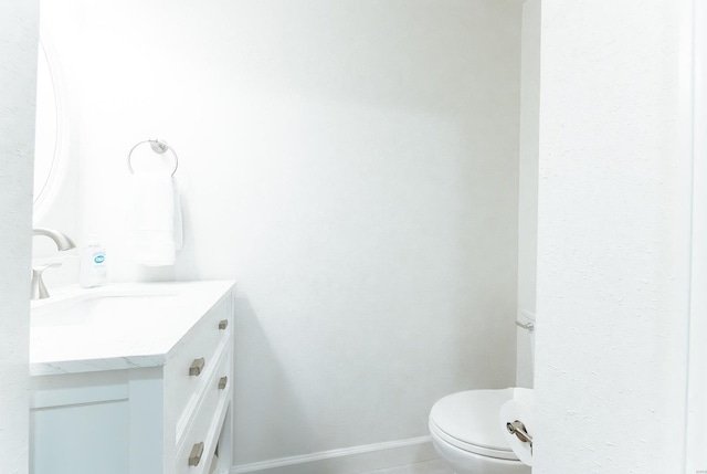 half bath with baseboards, vanity, and toilet