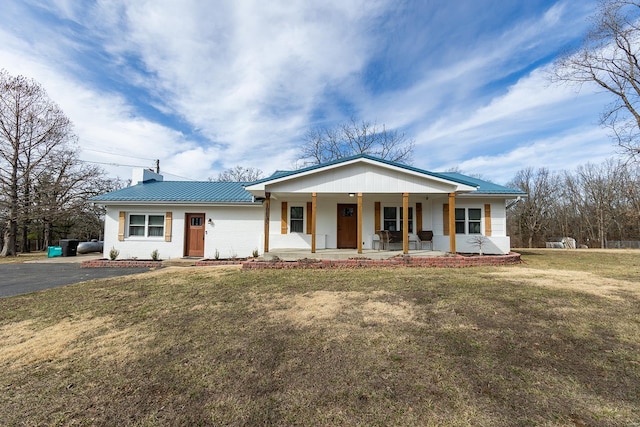 view of front facade featuring metal roof, a porch, a front yard, a standing seam roof, and a chimney