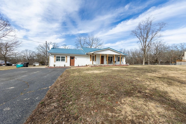 view of front of house featuring metal roof, aphalt driveway, a front lawn, and a porch