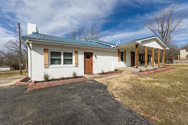 view of front of property featuring brick siding, a chimney, metal roof, a porch, and a front yard