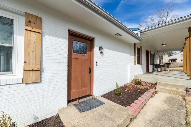 entrance to property featuring a porch and brick siding