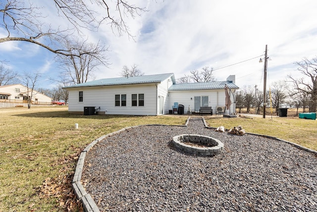 rear view of house featuring central AC, metal roof, a yard, and an outdoor fire pit