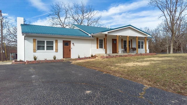 ranch-style house with covered porch, brick siding, metal roof, and a chimney