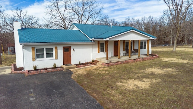 single story home with a chimney, metal roof, a front lawn, a porch, and brick siding