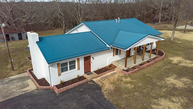 view of front facade featuring brick siding, metal roof, a chimney, and a front lawn