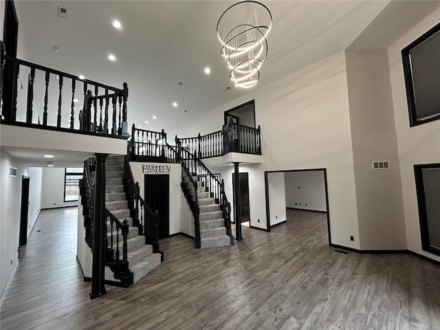 staircase featuring visible vents, a towering ceiling, an inviting chandelier, wood finished floors, and baseboards