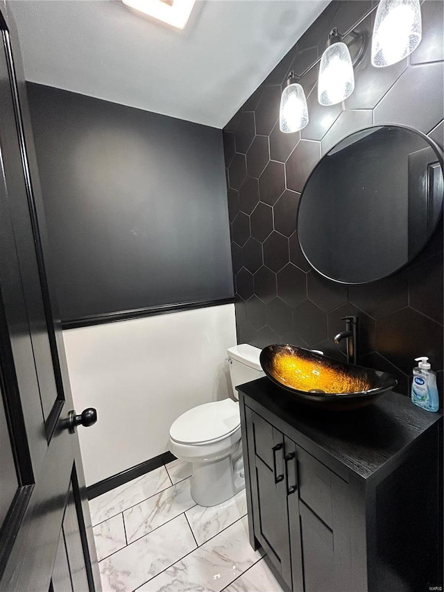 half bathroom featuring toilet, marble finish floor, tile walls, and vanity