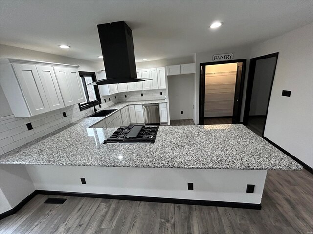 kitchen with light stone counters, a peninsula, island exhaust hood, stainless steel dishwasher, and a sink