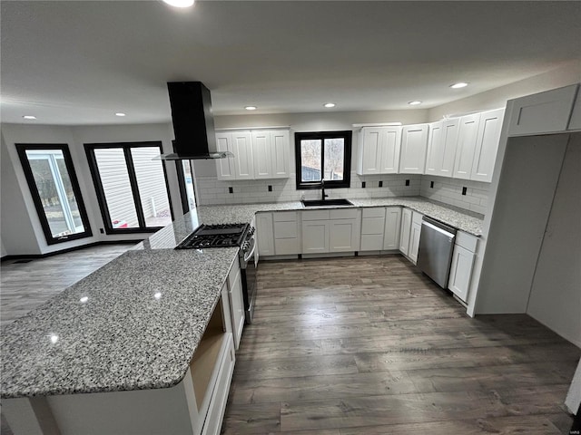 kitchen with appliances with stainless steel finishes, dark wood-style flooring, a peninsula, island exhaust hood, and a sink