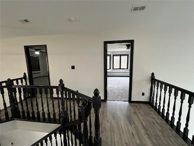 hallway with baseboards, visible vents, an upstairs landing, and wood finished floors