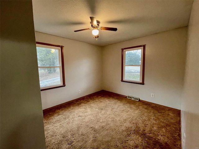 carpeted empty room featuring ceiling fan, plenty of natural light, and a textured ceiling