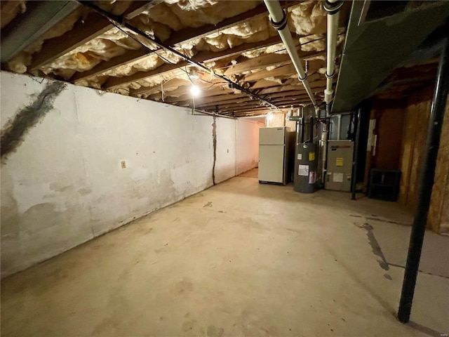 basement featuring heating unit and white fridge