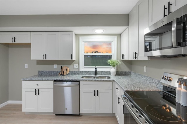 kitchen with white cabinetry, stainless steel appliances, light hardwood / wood-style flooring, light stone counters, and sink