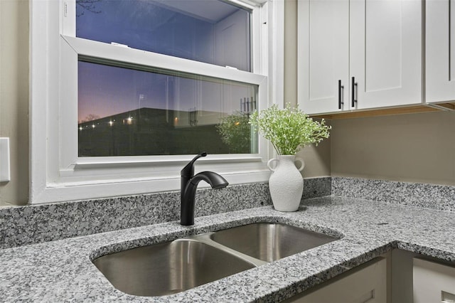 interior details featuring light stone countertops, sink, and white cabinets