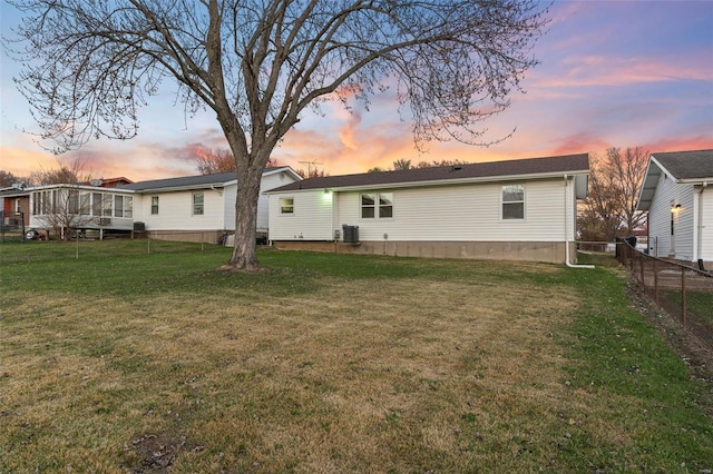 back house at dusk with a sunroom, a lawn, and central AC