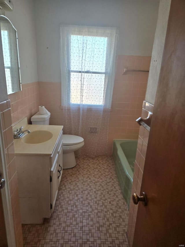 full bath with tile walls, a wainscoted wall, toilet, a tub to relax in, and vanity