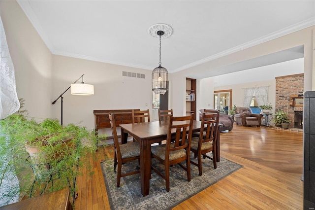 dining room featuring crown molding, a fireplace, hardwood / wood-style floors, and a notable chandelier