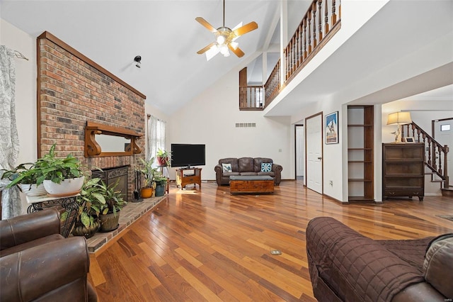 living room with hardwood / wood-style flooring, ceiling fan, a brick fireplace, and high vaulted ceiling