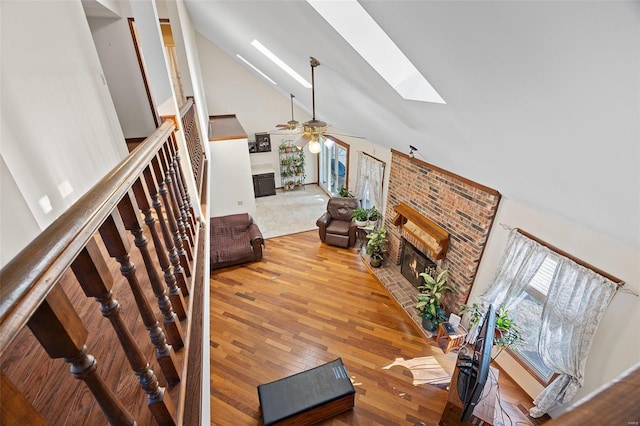 living room featuring hardwood / wood-style flooring, lofted ceiling with skylight, ceiling fan, and a fireplace