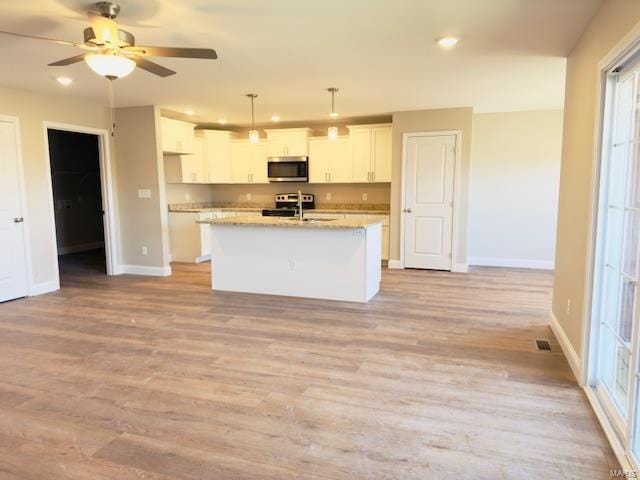 kitchen featuring white cabinetry, a kitchen island with sink, pendant lighting, light stone counters, and sink