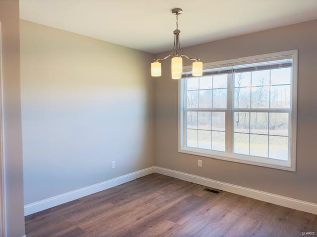 unfurnished room featuring plenty of natural light, an inviting chandelier, and hardwood / wood-style flooring