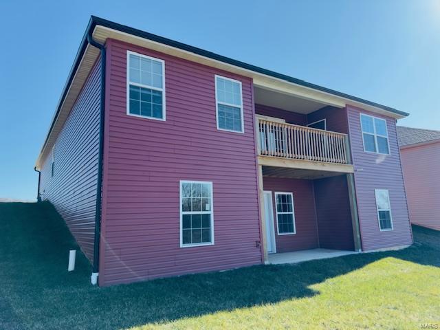 back of property featuring a balcony and a lawn