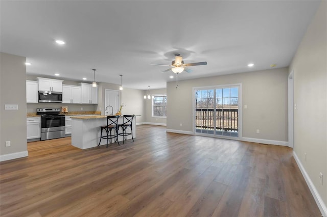 kitchen with a breakfast bar area, white cabinetry, hanging light fixtures, appliances with stainless steel finishes, and a kitchen island with sink