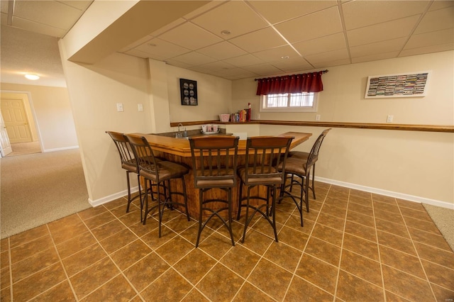 carpeted dining area featuring indoor bar and a paneled ceiling