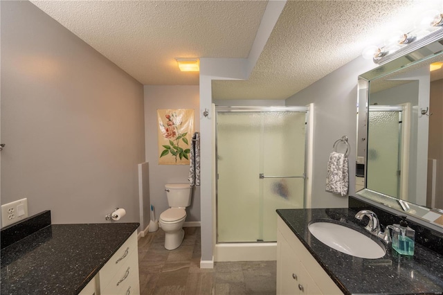 bathroom featuring vanity, toilet, a shower with door, and a textured ceiling