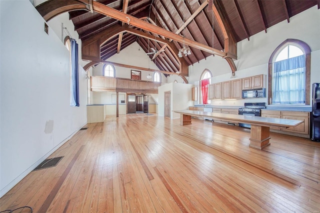 kitchen with gas stove, high vaulted ceiling, light hardwood / wood-style flooring, light brown cabinets, and beamed ceiling