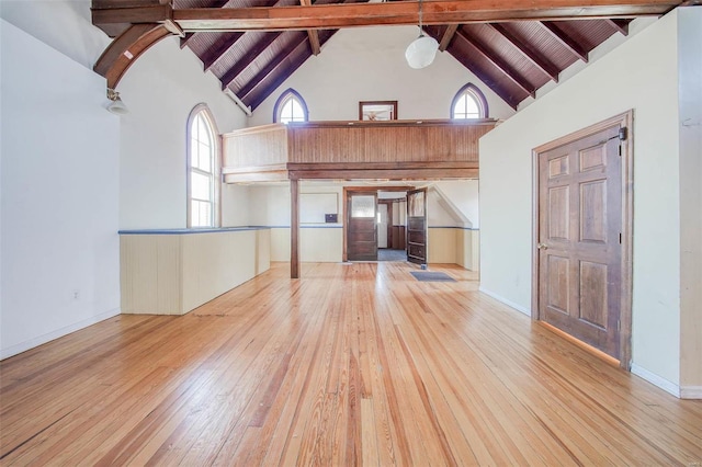 unfurnished living room featuring beam ceiling, high vaulted ceiling, and light hardwood / wood-style flooring