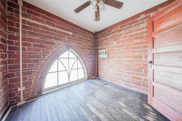 empty room featuring dark hardwood / wood-style flooring, a wall mounted air conditioner, ceiling fan, and brick wall