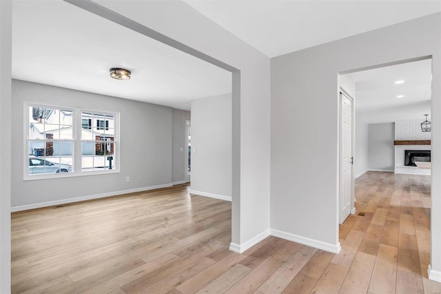 spare room with light wood-type flooring and a brick fireplace