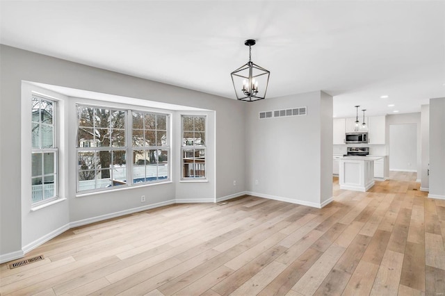 unfurnished dining area featuring an inviting chandelier and light hardwood / wood-style floors