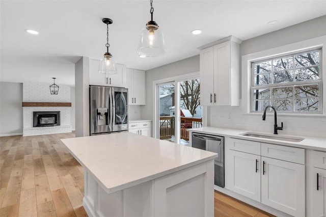 kitchen with white cabinetry, a center island, sink, appliances with stainless steel finishes, and pendant lighting