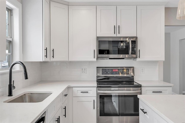 kitchen with white cabinetry, stainless steel appliances, sink, tasteful backsplash, and light stone counters