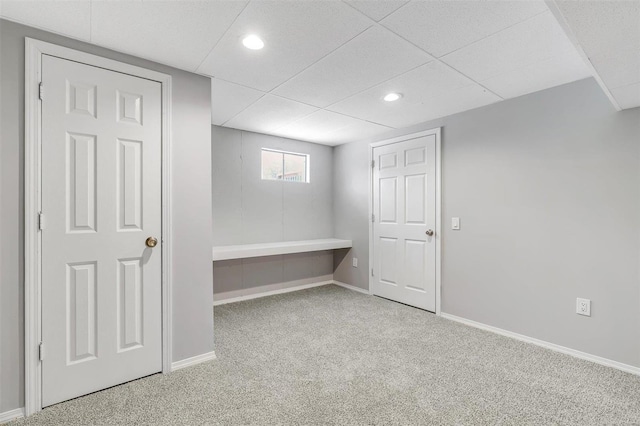 basement with a paneled ceiling and light colored carpet