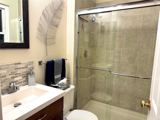 bathroom featuring a shower with door, toilet, vanity, and decorative backsplash