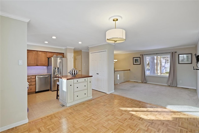 kitchen with pendant lighting, stainless steel appliances, crown molding, and a kitchen island with sink