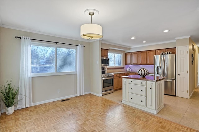 kitchen with crown molding, hanging light fixtures, appliances with stainless steel finishes, a kitchen island, and light parquet floors