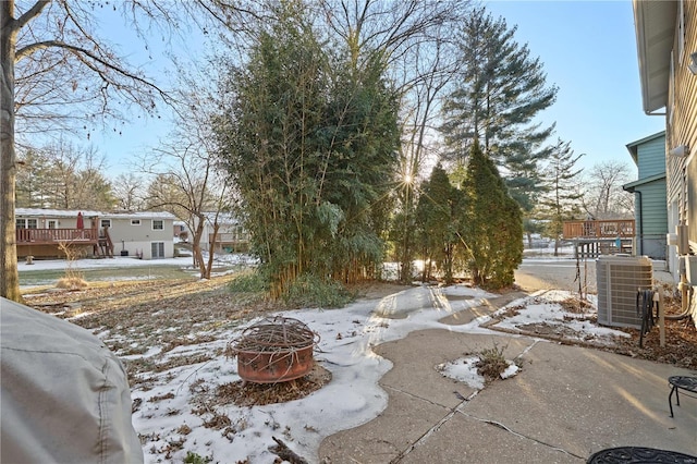 yard covered in snow featuring cooling unit, a wooden deck, and an outdoor fire pit