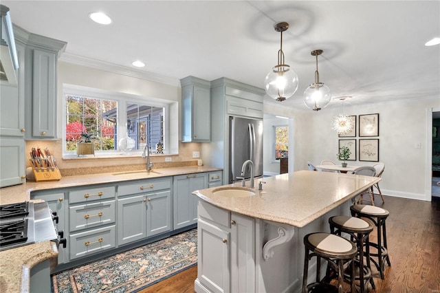 kitchen with decorative light fixtures, sink, a kitchen island with sink, and stainless steel refrigerator